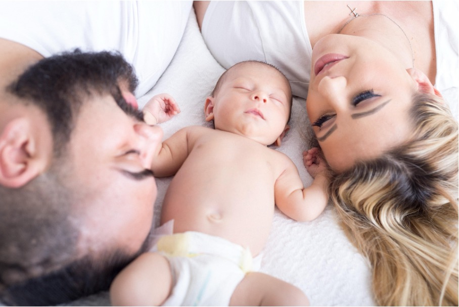 Mutter, Vater und Neugeborenes liegen kuschelnd zusammen